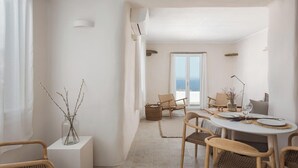 A dining area with a round table, wicker chairs, and a view of the sea through a large window. - Green 3, Morfes Luxury Apartments (Tinos)