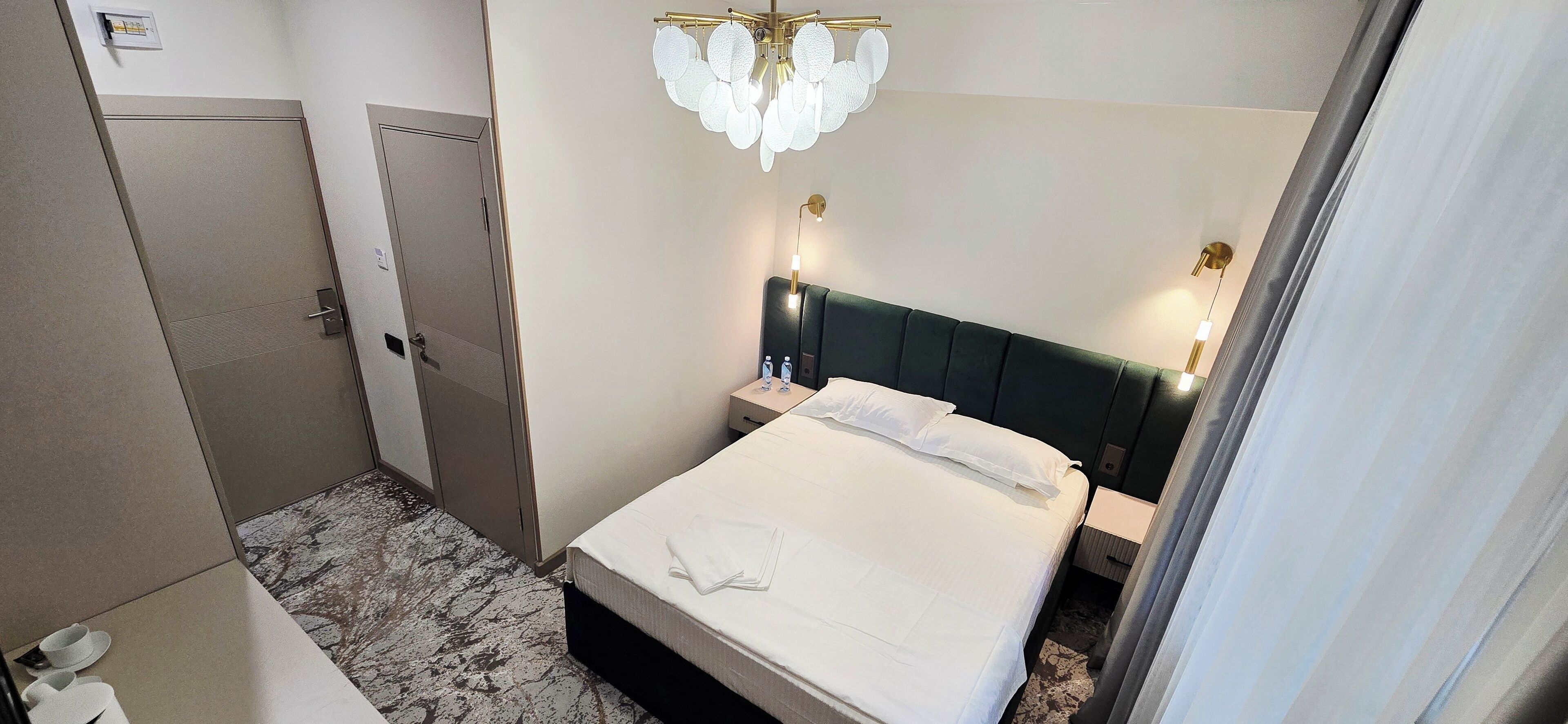 Ein Hotelzimmer mit Bett, Nachttischen, einer Chandelierleuchtre und einer Tür.