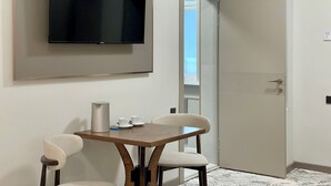 A modern room with a flat-screen TV mounted on the wall, a wooden table with two chairs, and a door leading to a balcony. - Naya Hotel (Almaty)