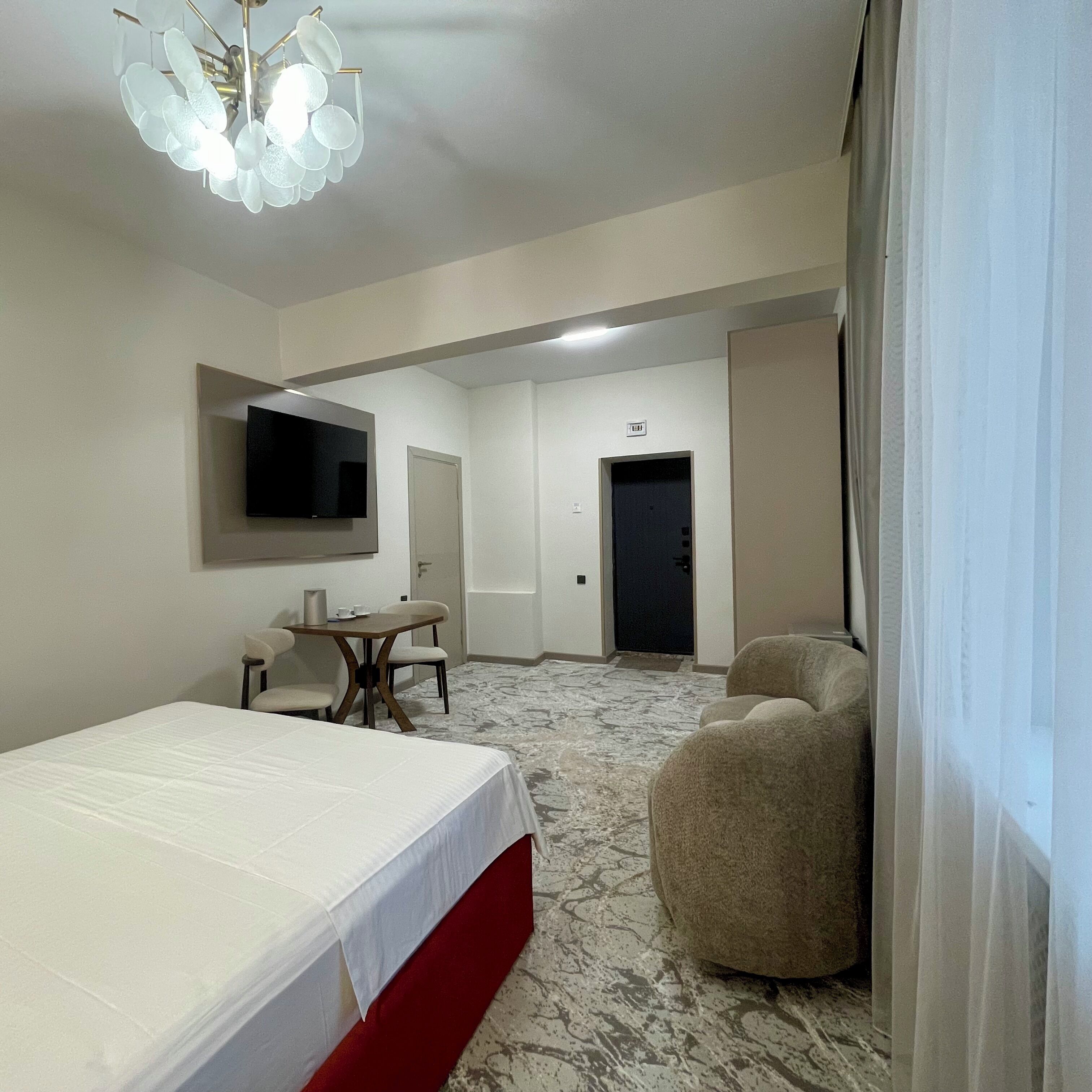A hotel room with a bed, a TV mounted on the wall, a desk with chairs, and a door leading to another room.