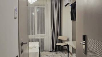 Una habitación de hotel con cama, una silla, un escritorio, televisor y ventana con cortinas.