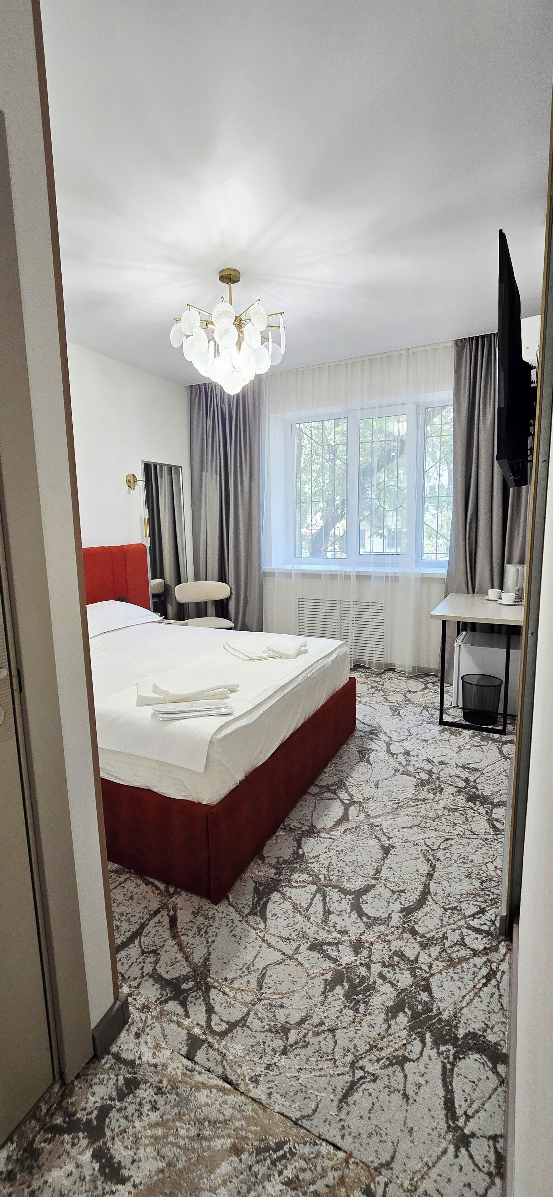 Een hotelkamer met een groot bed, een televisie, een bureau met stoel, en een raam met gordijnen.
