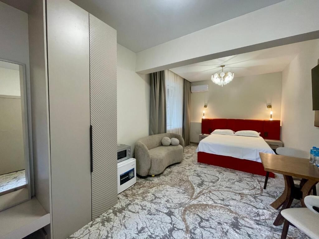 A hotel room with a bed, a sofa, a dining table, and a minibar.