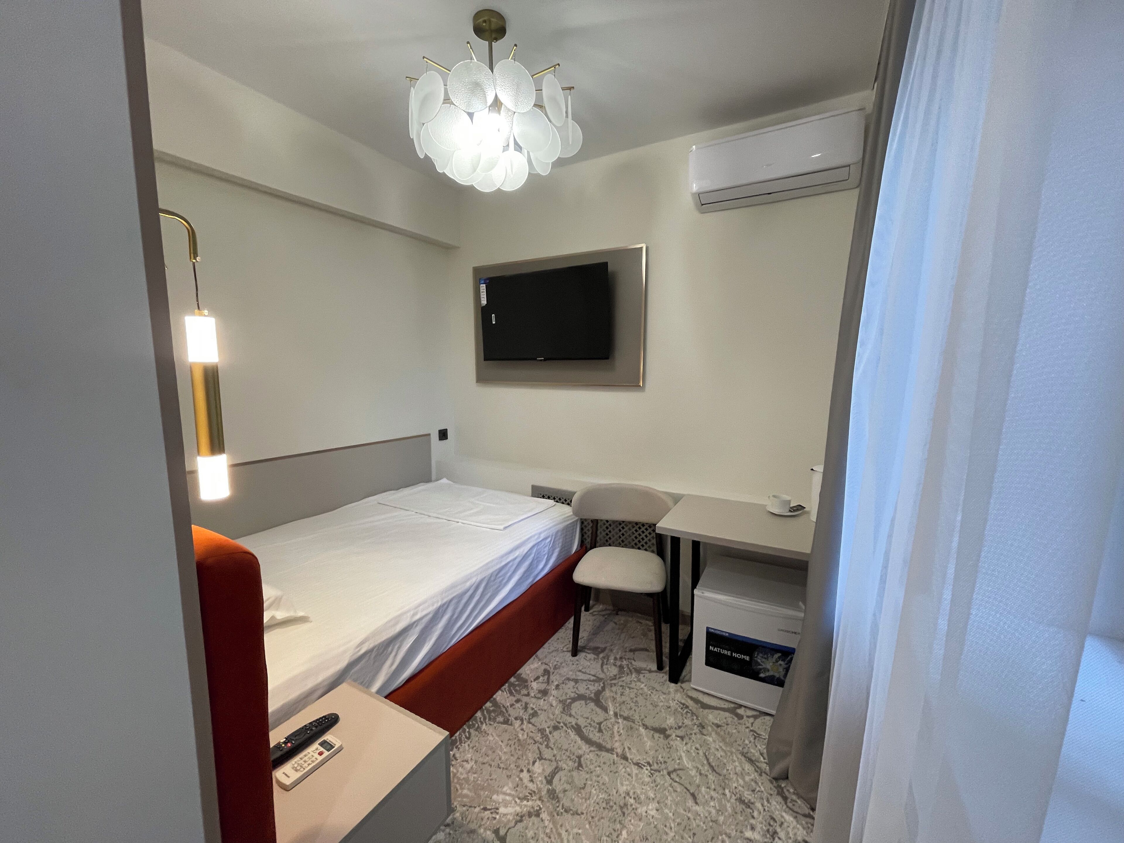 A hotel room with a bed, a desk, a chair, a television, and an air conditioning unit.