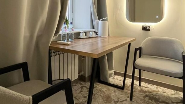 A room with a wooden desk, two chairs, a large mirror, and a window with curtains. - Naya Hotel (Almaty)