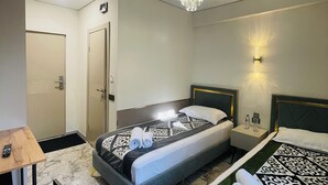 A hotel room with two beds, a chandelier, a nightstand with a lamp, and a door. - Naya Hotel (Almaty)