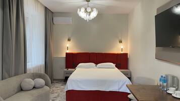 Habitación de hotel con cama, sofá, mesa de comedor, televisor y candelabro.