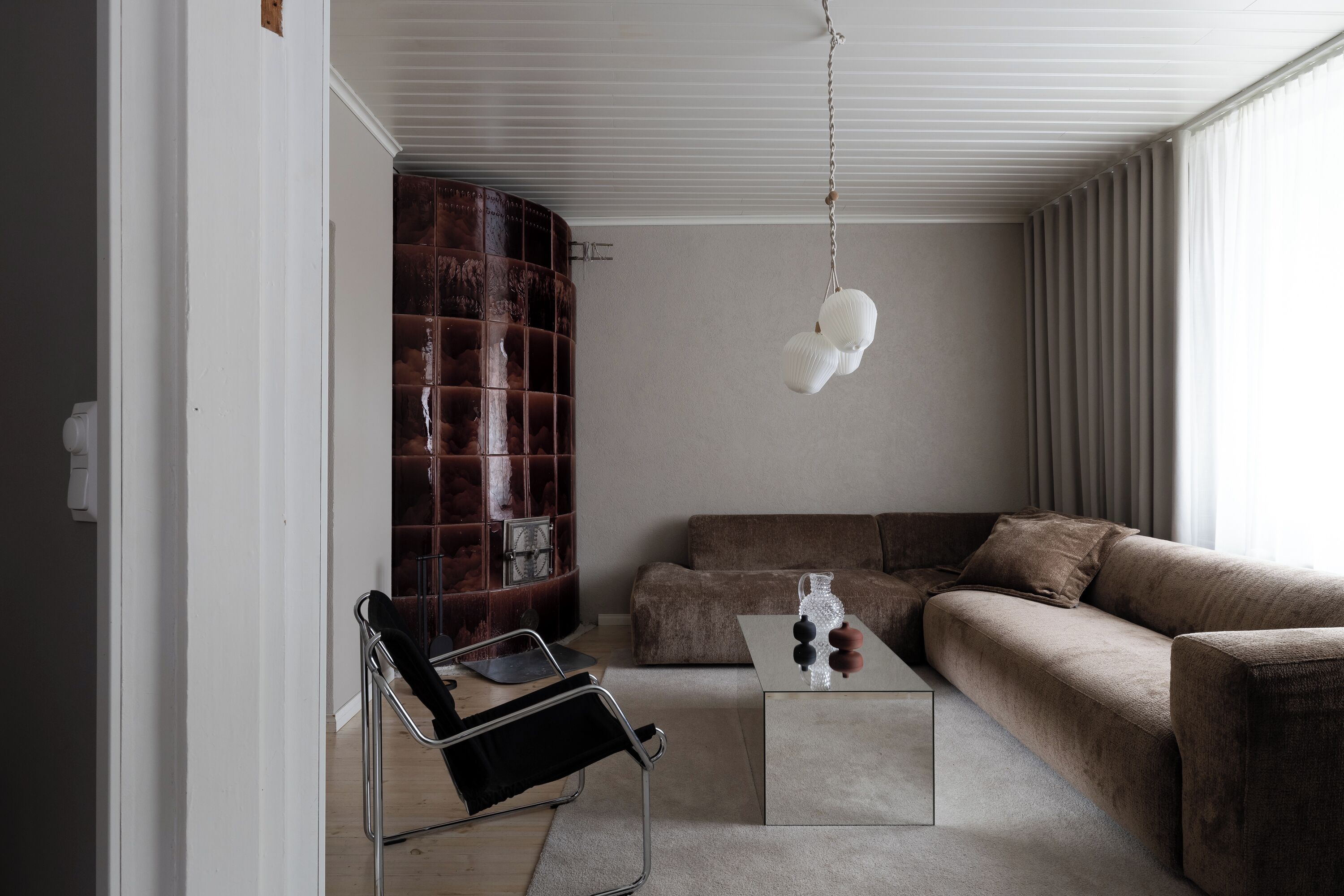 Una sala de estar moderna con un sofá marrón, una silla negra, una mesa de centro de vidrio y una lámpara colgante.