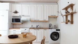A modern kitchen with white cabinets, a microwave, a washing machine, and a wooden dining table. - Stylish 1BR Apt. in Historic Area (Tampere)