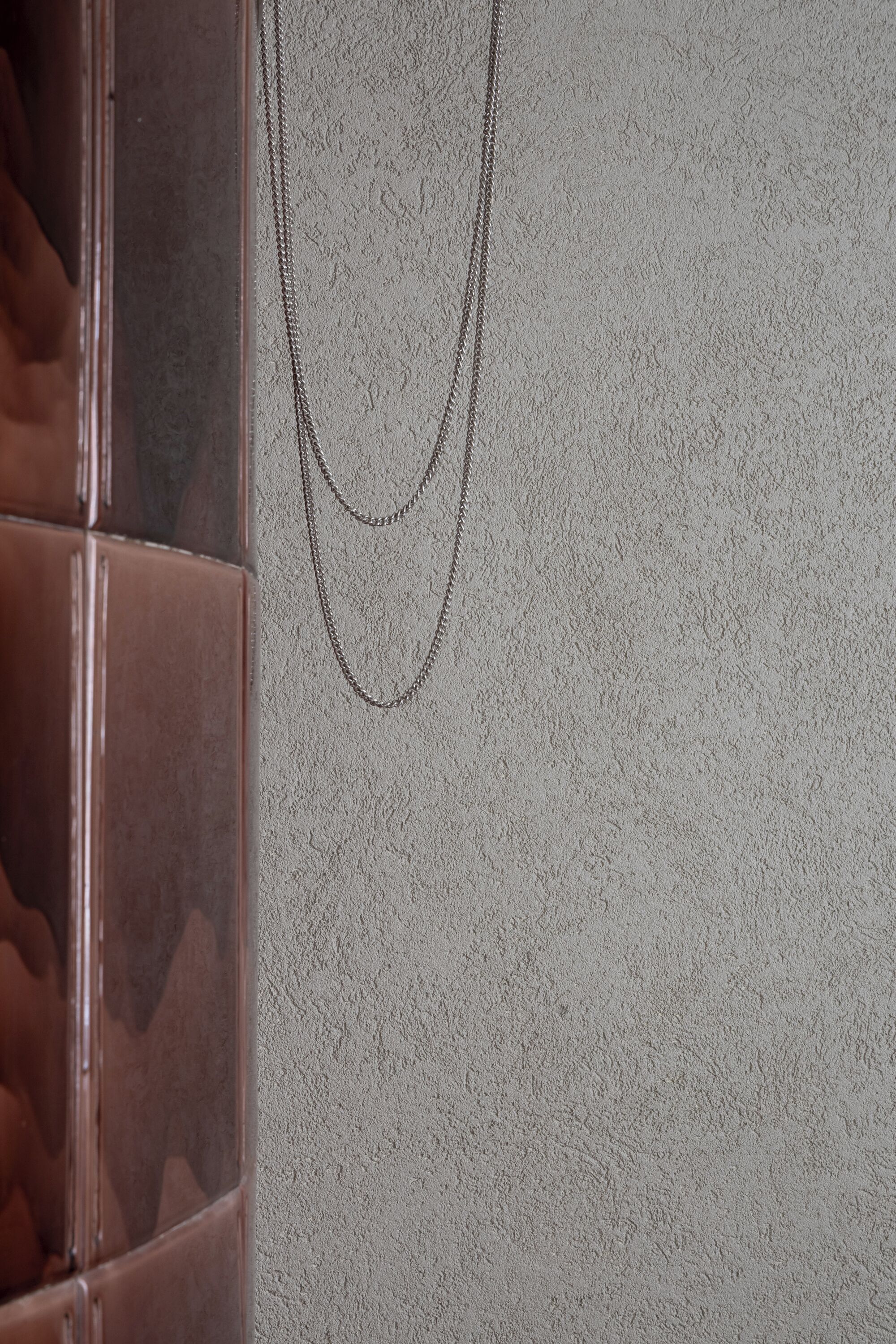 A textured wall with a double-layered chain hanging from it.