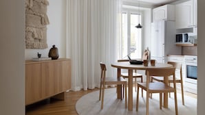 A modern kitchen with white cabinets, a wooden dining table, and a large window with sheer curtains. - Stylish 1BR Apt. in Historic Area (Tampere)