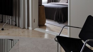 A modern hotel room with a bed, a black chair, a TV, and a large window with curtains. - Stylish 1BR Apt. in Historic Area (Tampere)