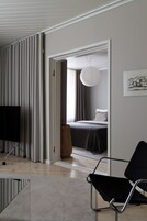 A modern hotel room with a bed, a black chair, a TV, and a large window with curtains.