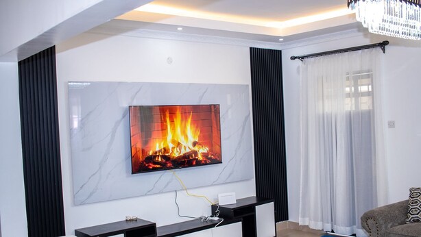 Ett modernt vardagsrum med en platt-TV som är monterad på en vägg av marmor, ett svart konsolbord och en grå soffa.