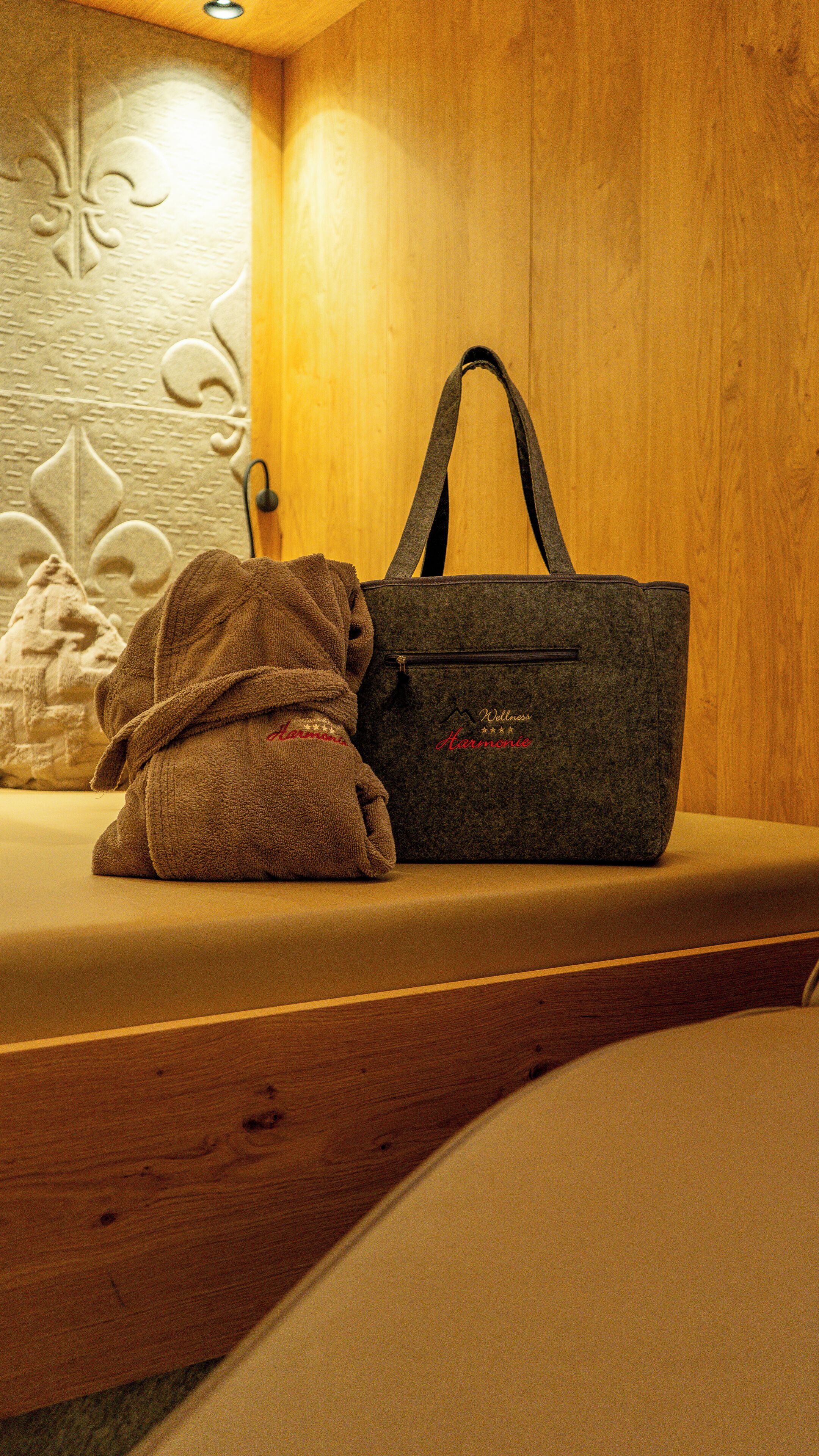 Un banco de madera con una toalla y una bolsa gris oscuro con el texto grabado 'Wellness Harmony'.