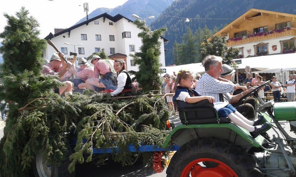 Um grupo de pessoas em um trator verde carregando um carregamento de árvores de Natal.