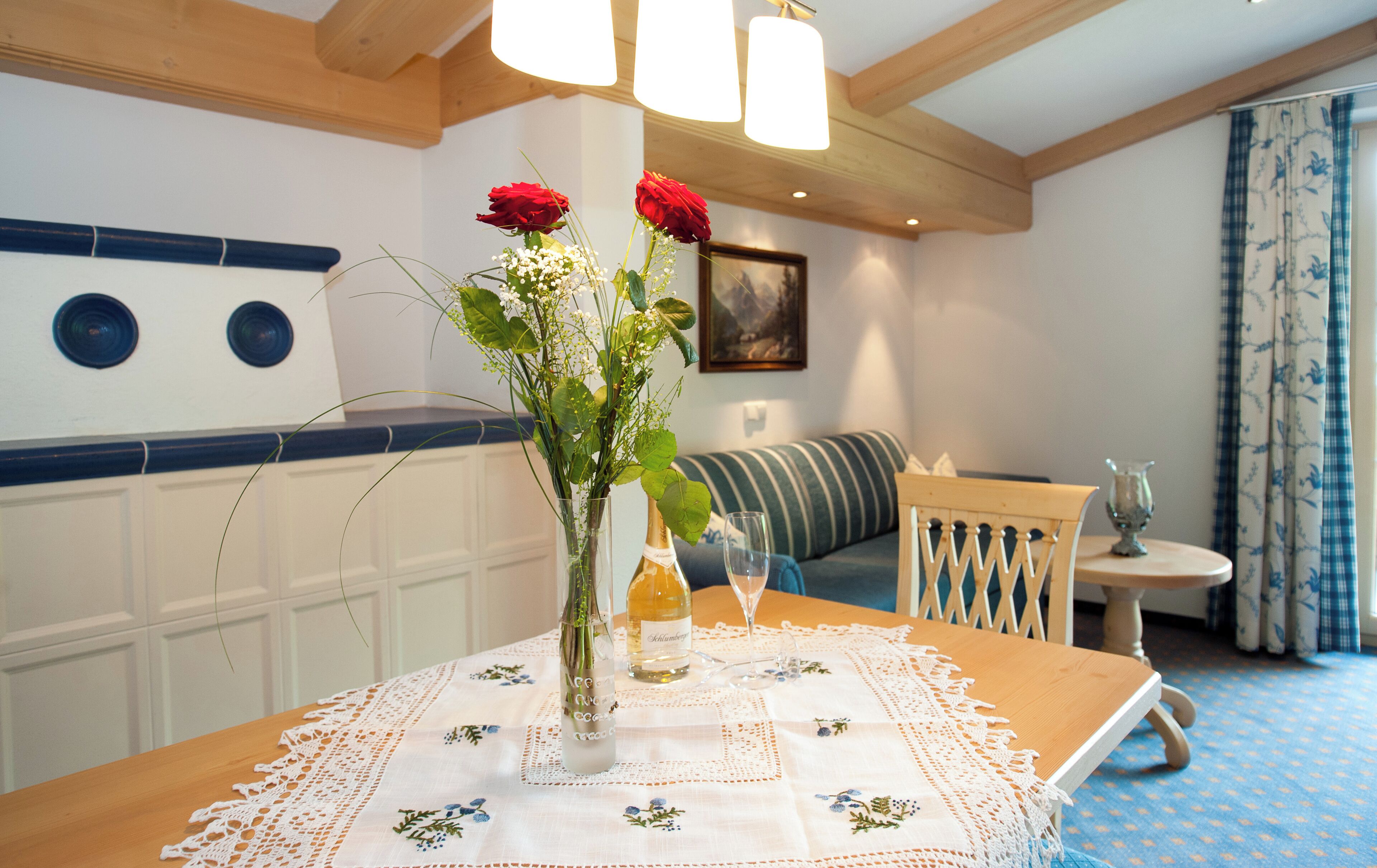 A dining table with a lace tablecloth, a vase with flowers, and a bottle of wine.