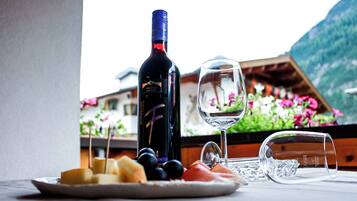 A wine bottle, a wine glass, and a plate with cheese and fruit on a table with a mountain view.