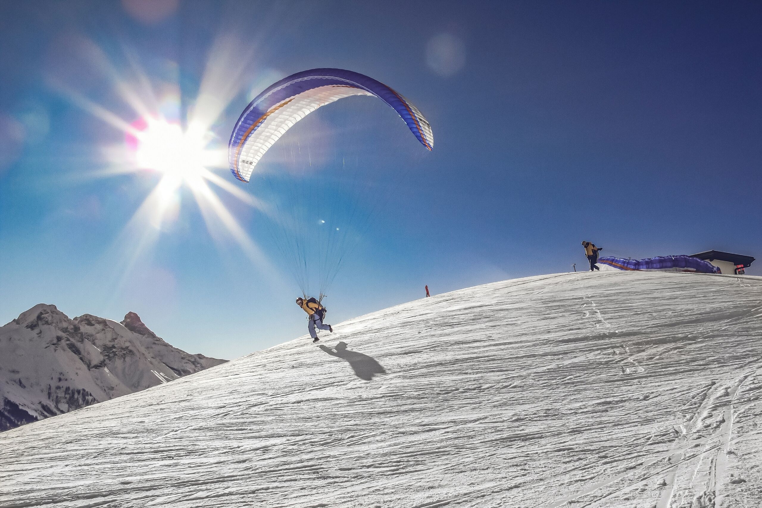 A snowy mountain slope with a person paragliding.