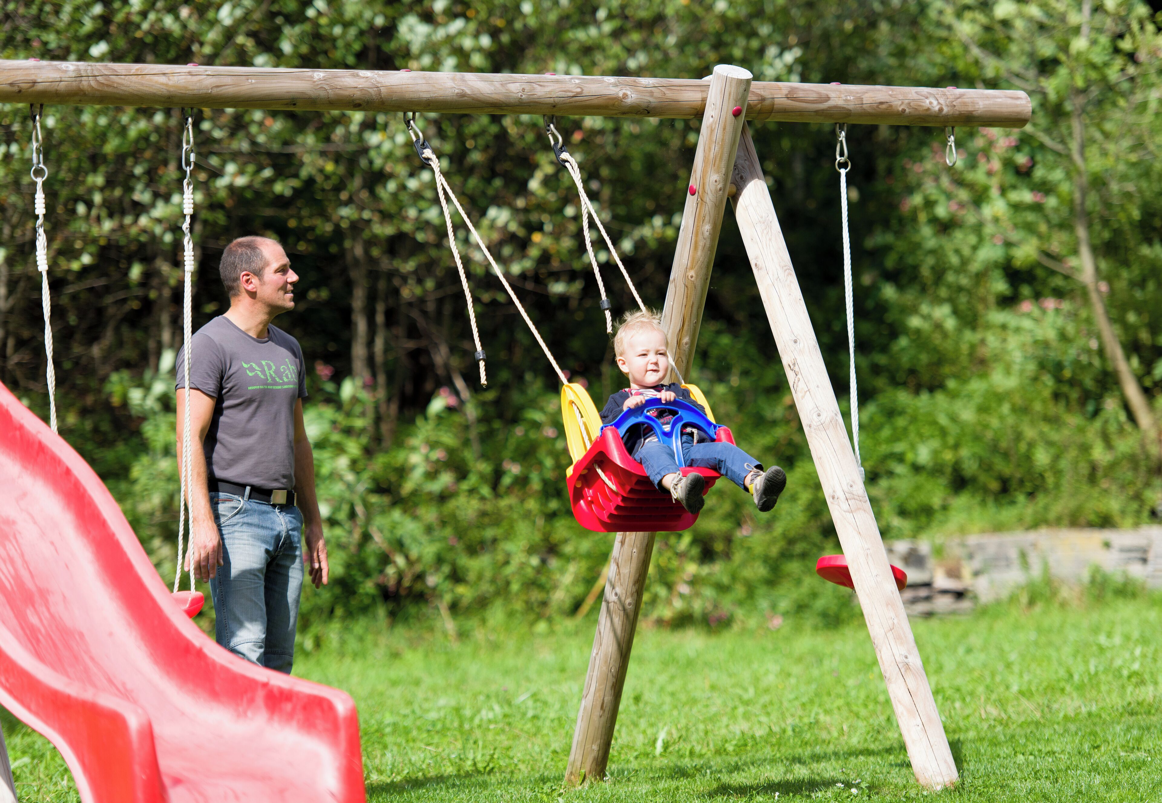 A wooden swing set with a red slide in a grassy park area.