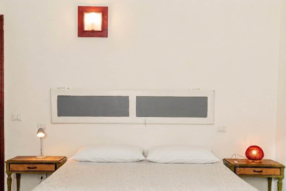 Una camera da letto essenziale con un letto, due comodini e una lampada a parete.