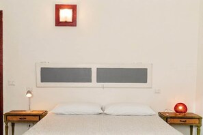 A simple bedroom with a bed, two bedside tables, and a wall-mounted light fixture. - Panoramic Terrace & Comfort in the Heart of Todi (Todi)