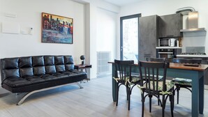 A modern living room with a black leather sofa, dining table with chairs, and a kitchen area with a microwave and stove. - Todi center -Elegant apartment with Spectacular View. Unmissable Terrace! (Todi)