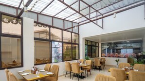 A restaurant with multiple tables and chairs, large windows, and a high ceiling with a skylight. - Hotel Pride  (Gangtok)