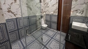 A bathroom with a glass-enclosed shower, a toilet, and a sink. - Modern Comfort in the Heart of the City – Spacious Rooms & Top Amenities (agra)