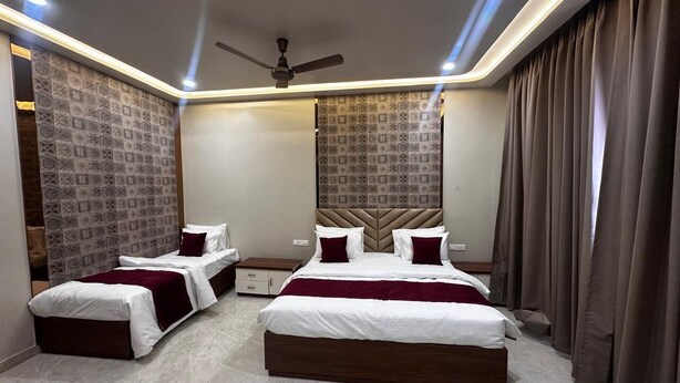 A modern bedroom with two beds, a ceiling fan, patterned wallpaper, and a large window with curtains. - Modern Comfort in the Heart of the City – Spacious Rooms & Top Amenities (agra)