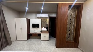 A hotel room with a bed, a desk, a TV, and a wardrobe. - Modern Comfort in the Heart of the City – Spacious Rooms & Top Amenities (agra)