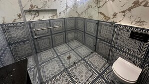 A bathroom with a glass-enclosed shower, patterned tiles, and a white toilet. - Modern Comfort in the Heart of the City – Spacious Rooms & Top Amenities (agra)