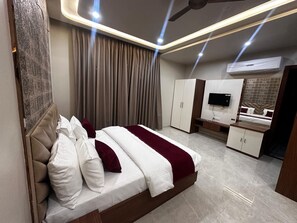 Quarto de hotel moderno com uma cama grande, televisão, guarda-roupa e ventoinha de teto.