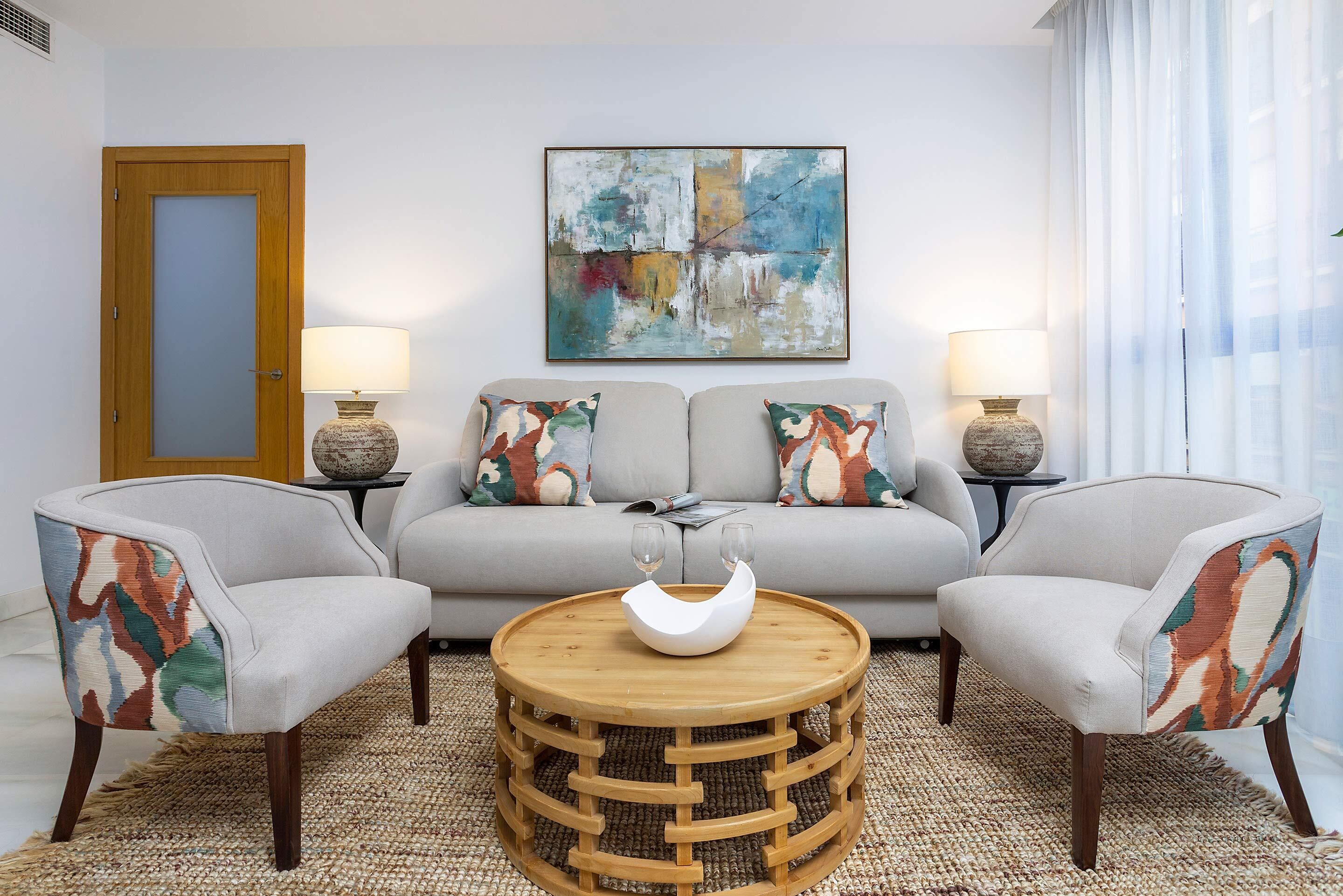 Un salon comprenant un canapé, deux fauteuils, une table basse ronde en bois et deux lampes.