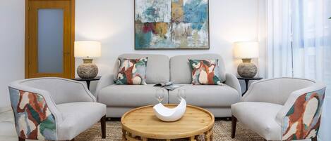 A living room with a sofa, two armchairs, a round wooden coffee table, and two lamps.