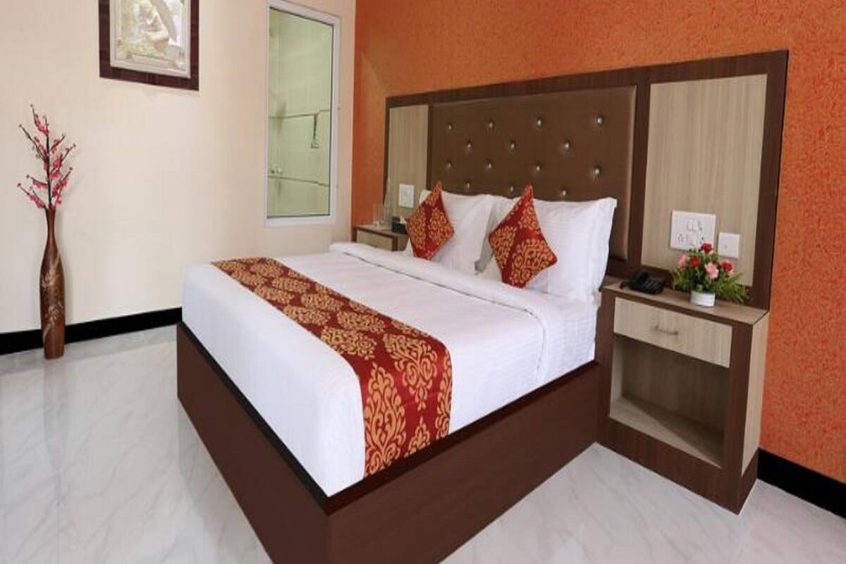A hotel room with a large bed, a nightstand, a mirror, and a vase with flowers.