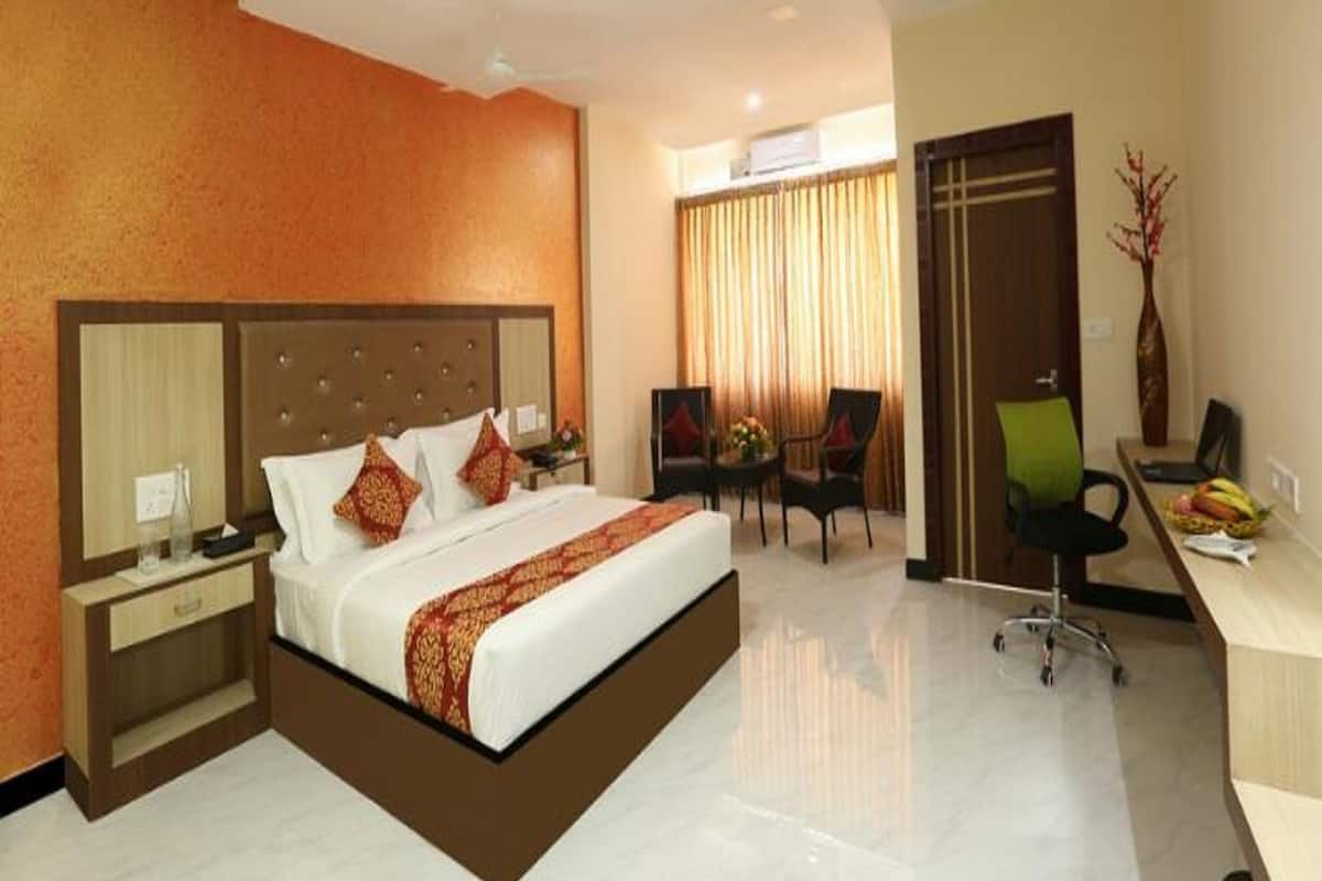 A hotel room with a large bed, a desk, a chair, and a small table.