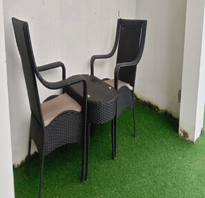Two wicker chairs with cushioned seats and backs, positioned on a patch of artificial green grass against a white wall. - TNV Casita Inn (Yercaud)