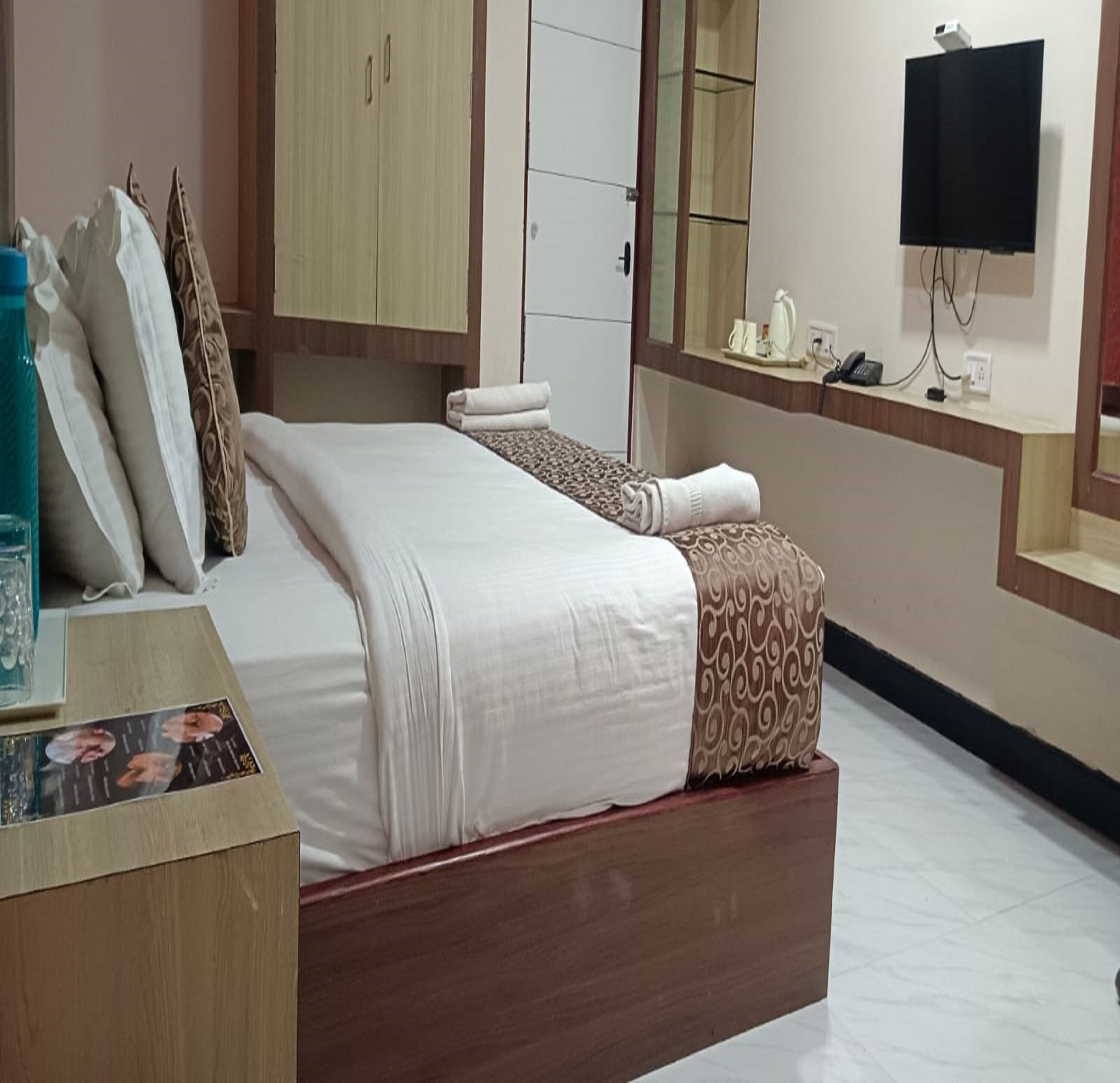 A hotel room with a bed, a desk, a mirror, a TV, and a wardrobe.