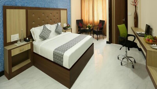 Une chambre d’hôtel avec un grand lit, un bureau avec une chaise, une petite table avec des chaises et une porte.