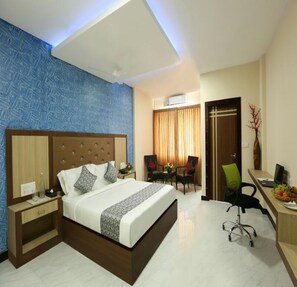 A hotel room with a large bed, a desk with a chair, a small table with chairs, and a door. - TNV Casita Inn (Yercaud)