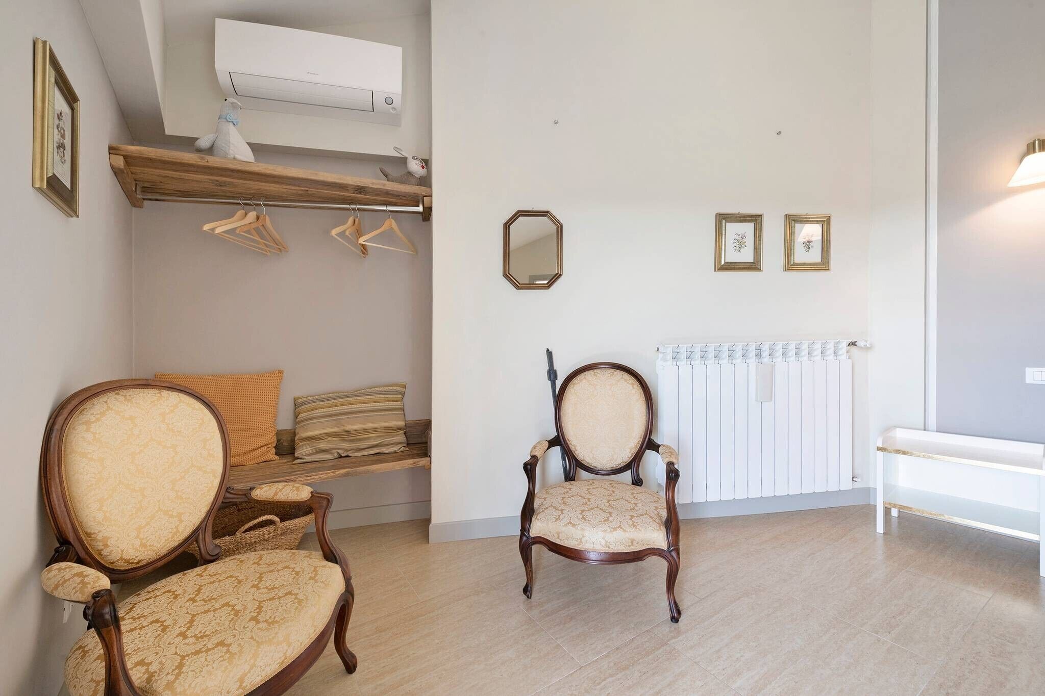 A room with a wooden chair, a bench, a radiator, and a wall-mounted mirror.