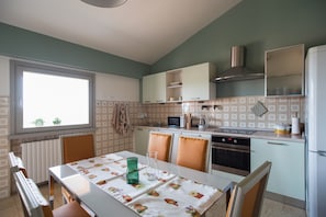 Een keuken met een eettafel, stoelen, een raam en een magnetron.