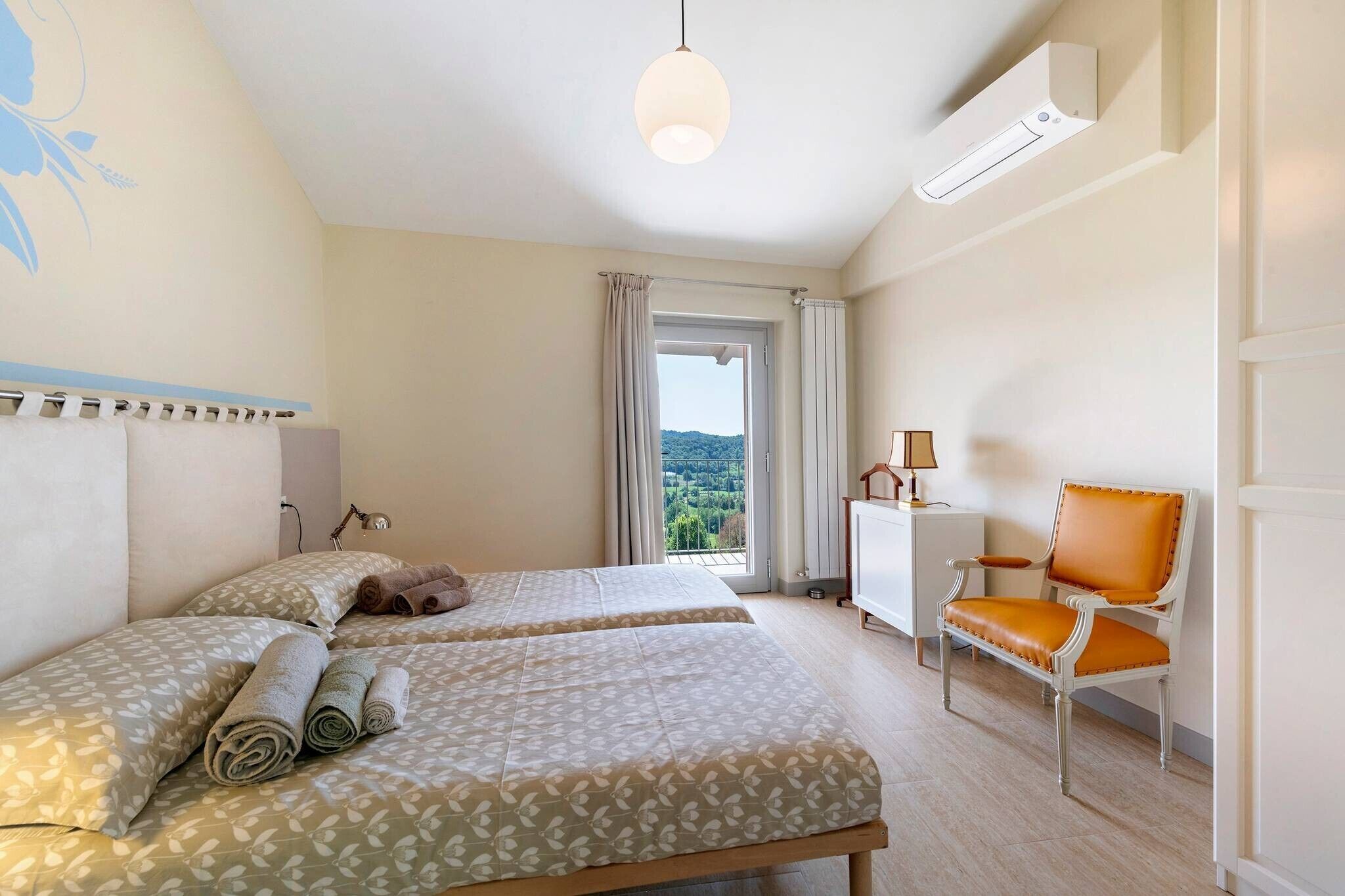 Ein Hotelzimmer mit zwei Betten, einem Sessel, einem Schreibtisch und Blick ins Freie.