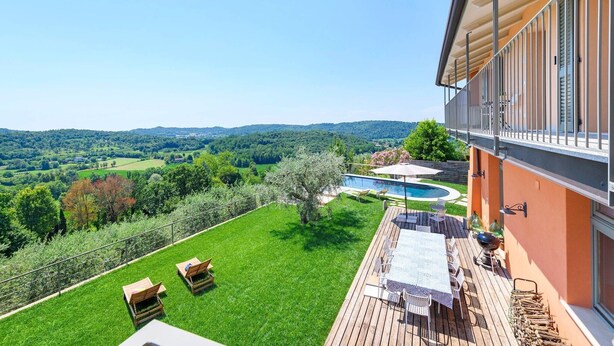 Ein Balkon mit Blick auf einen Swimmingpool, eine Rasenfläche und eine Holzterrasse mit Gartenmöbeln.