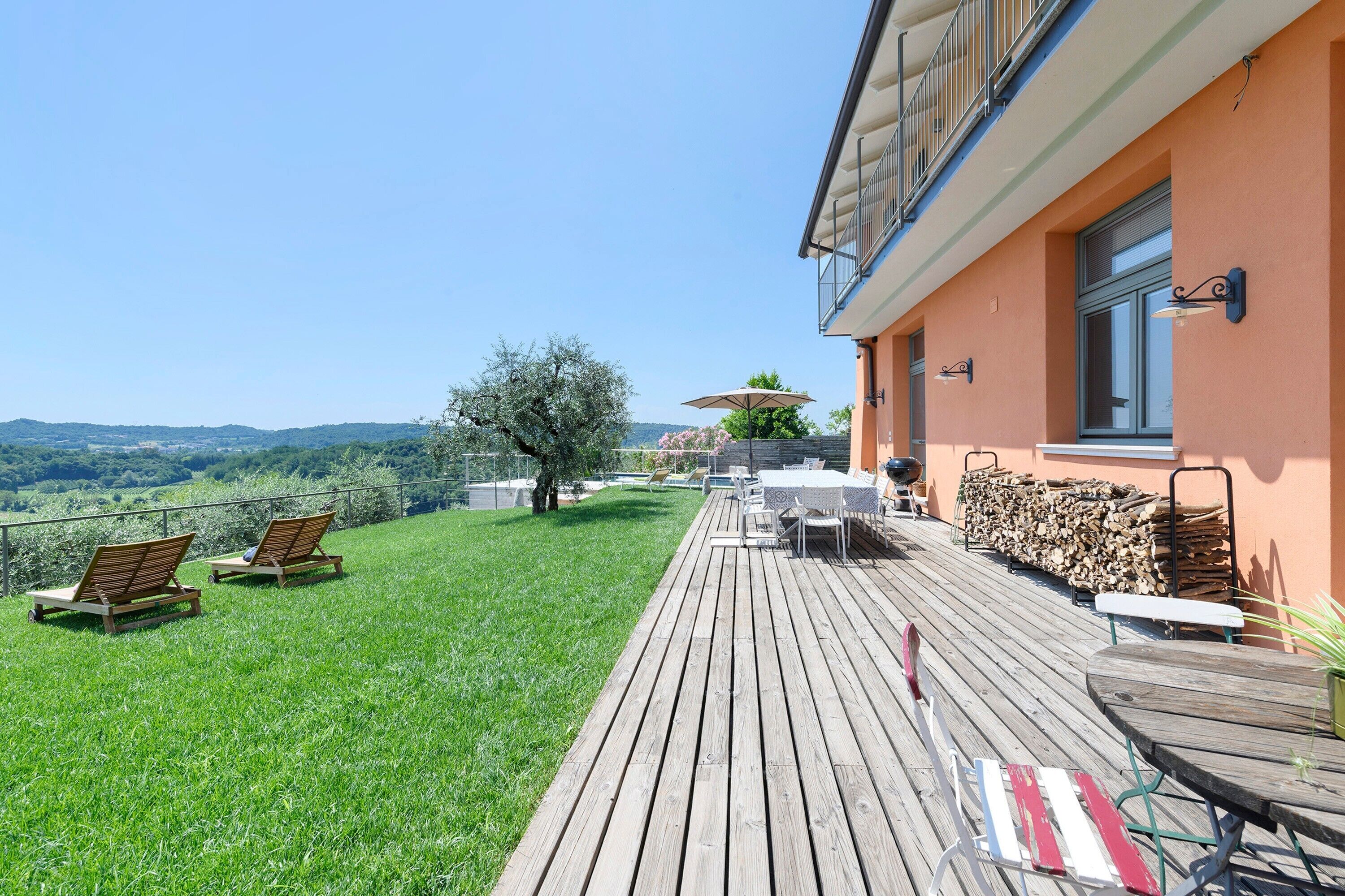 Eine Terrasse mit Gartenmöbeln, Blick auf die Landschaft und ein Gebäude mit Balkon.