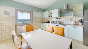 Eine Küche mit Esstisch, Stühlen, einem Fenster und Blick ins Freie.