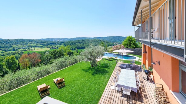 Ein Balkon mit Blick auf einen Swimmingpool, eine Rasenfläche und eine Holzterrasse mit Gartenmöbeln.