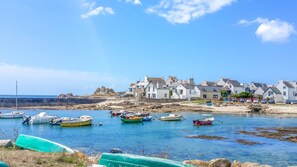 Uma vila costeira com casas ao longo da praia, barcos na água e céu claro.