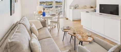 A modern living room with a sofa set, a dining table, and a kitchen area with a TV.